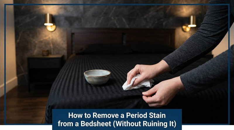 Hand treating a stain on a black bedsheet with a cloth