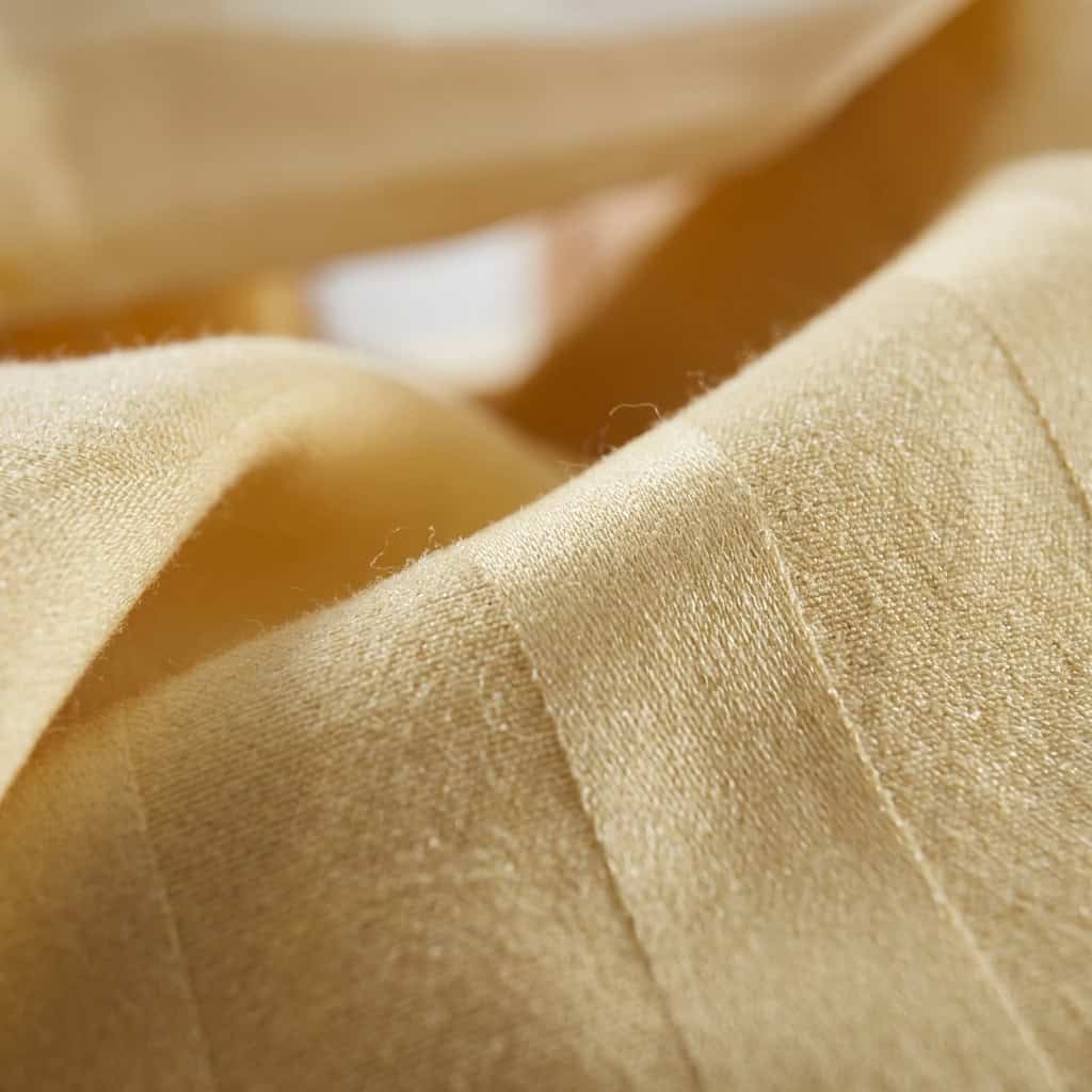 Close-up of butter yellow cotton bedsheet fabric with a subtle stripe weave