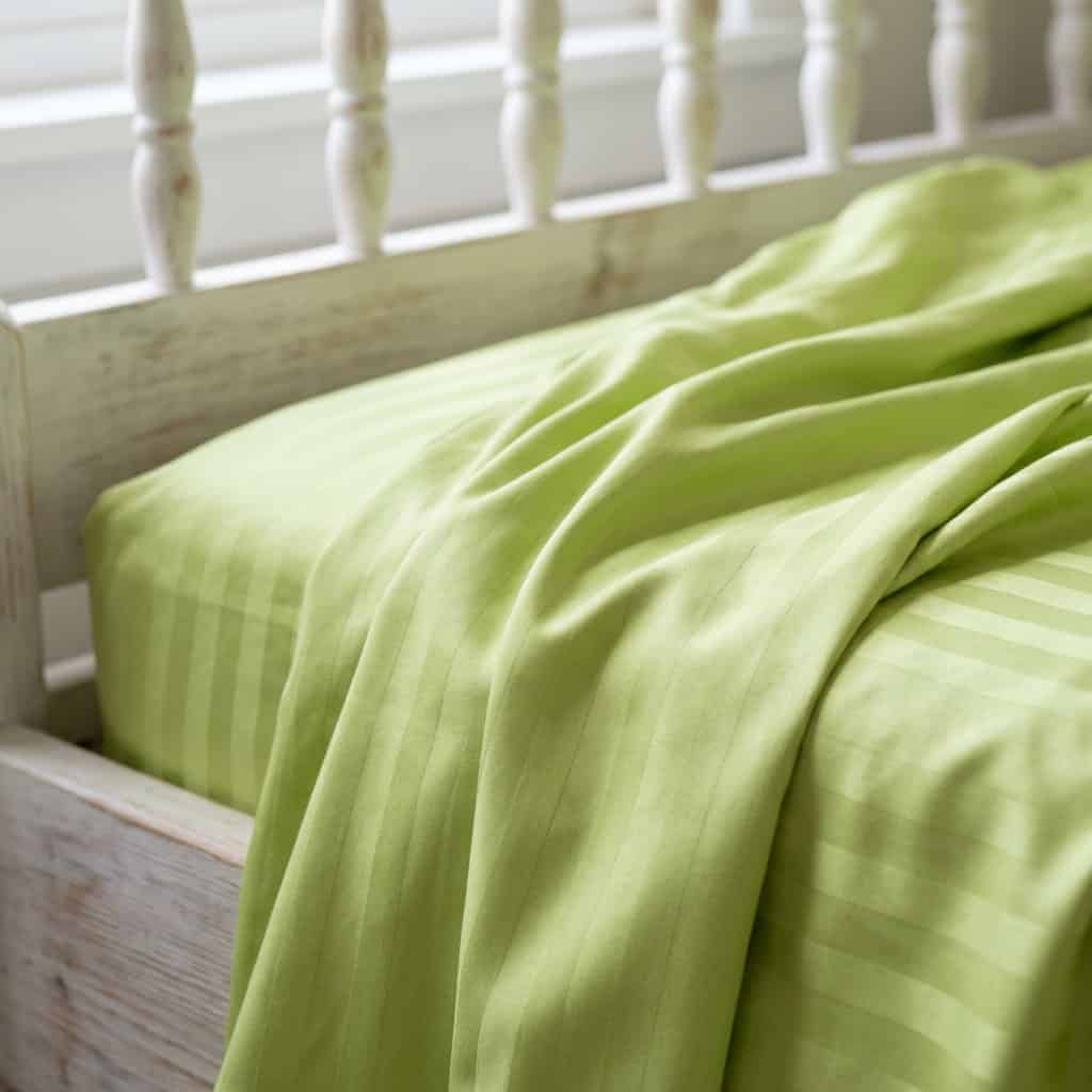 Close-up of lime green cotton bedsheet fabric with a subtle stripe weave