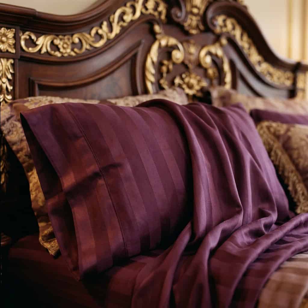 Close-up of plum cotton bedsheet fabric with a subtle stripe weave